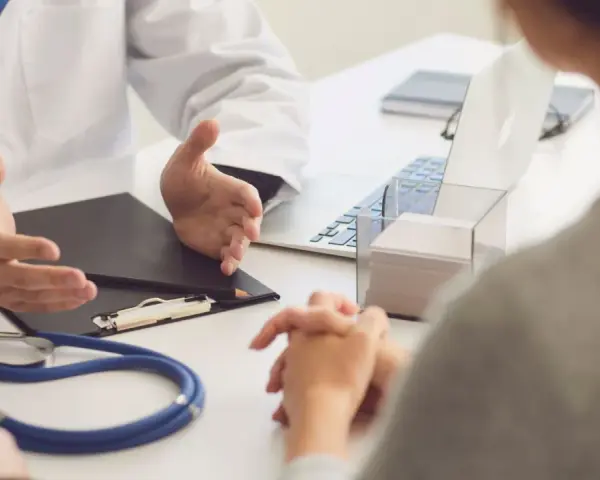Lekarz omawia z pacjentem diagnozę, być może f43 kod choroby. Na stole stetoskop i laptop.