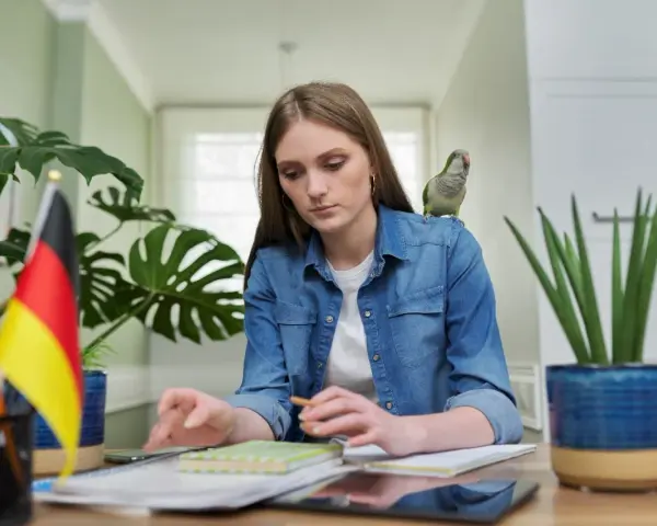 Dziewczyna z papugą na ramieniu uczy się niemieckiego. Może szuka inspiracji na piosenkę na urodziny po niemiecku?