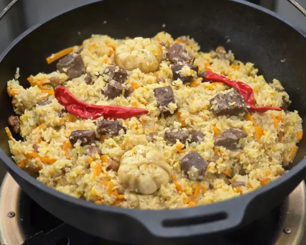 Herzhaftes Plov-Rezept im Kessel: Reis, Fleisch, Karotten, Knoblauch und scharfe Chilis. Ein Festmahl!