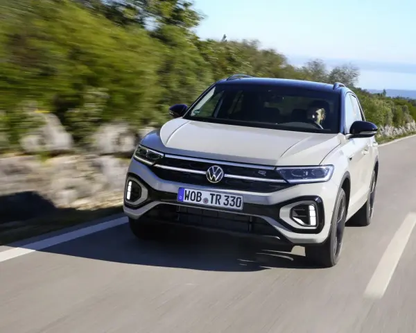 Jasnoszary Volkswagen T-Roc jedzie po krętej drodze. Nawet przy potencjalnych usterkach, ten model prezentuje się dynamicznie.