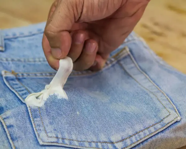 Mano quitando chicle pegado en bolsillo de jeans. Aprende como quitar chicle de la ropa fácilmente.