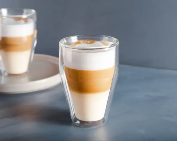 Dwa latte macchiato w szklankach z podwójnymi ściankami, z wyraźnie widocznymi warstwami mleka i kawy.