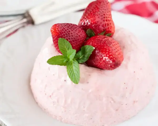 Deliziosa bavarese alle fragole, guarnita con fragole fresche e menta, su un piatto bianco.