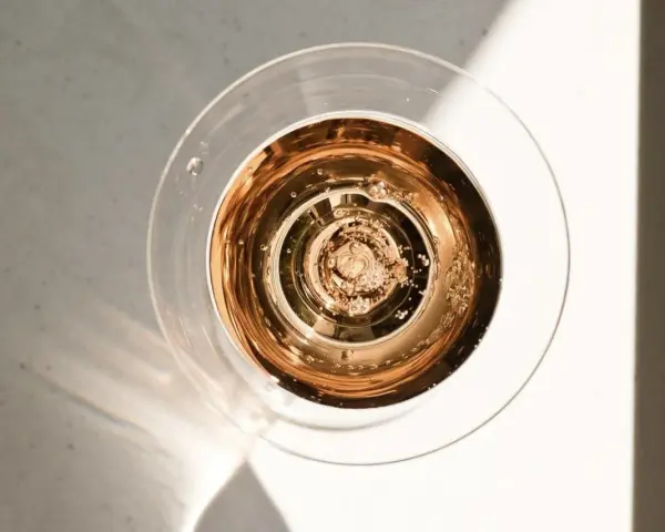 Szklanka z różowym, musującym winem, które wygląda jak tanie wino, ale jest podane w elegancki sposób. Bąbelki unoszą się ku górze.