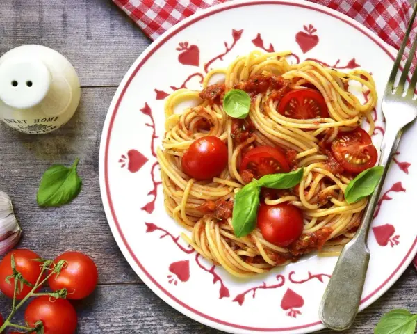 Makaron spaghetti z sosem pomidorowym, pomidorkami koktajlowymi i bazylią na talerzu.