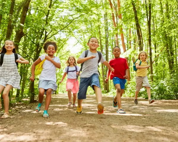Des enfants joyeux, des supernova juniors, courent sur un sentier forestier ensoleillé, pleins d'énergie.