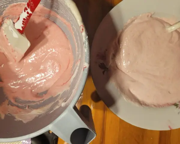 Różowa masa na makaroniki w misce i na talerzyku. Szpatułka miesza kremową konsystencję. Idealny makaroniki przepis w przygotowaniu.
