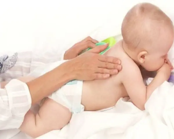 Dziecko w pieluszce leży na brzuchu, a dorosły delikatnie masuje mu plecy.