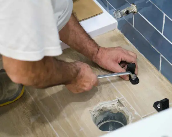 A person uses a wrench to tighten a toilet flange bolt, demonstrating how to replace a toilet flange.