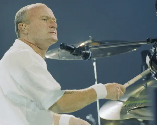 Phil Collins, w białej koszuli, gra na perkusji. Legendarny muzyk, znany z zespołu Genesis.