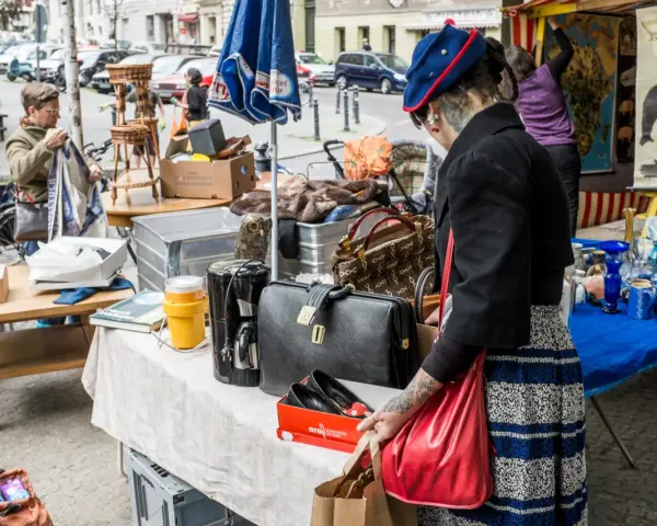 Frau mit Tätowierungen auf dem Arm sucht auf einem antik flohmarkt nach Schätzen. Sie hält eine rote Tasche.