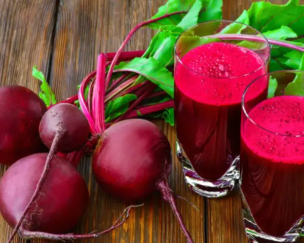 Frische rote Bete und zwei Gläser mit leuchtend rotem Rote-Bete-Saft stehen auf einem Holztisch.