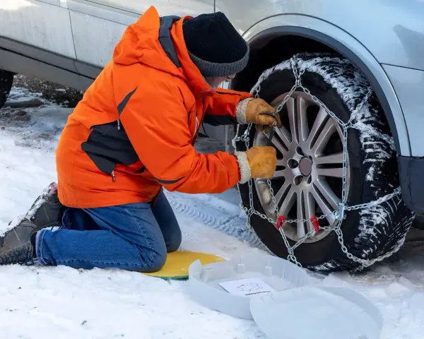 Uomo in giacca arancione monta catene da neve su ruota posteriore. Le catene da neve devono essere montate sulle ruote posteriori per la massima aderenza.