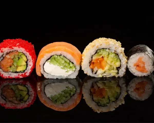 Różne rodzaje sushi: rolka z łososiem i awokado w ikrze, z łososiem i serkiem, z sezamem i warzywami, oraz klasyczne maki z łososiem.