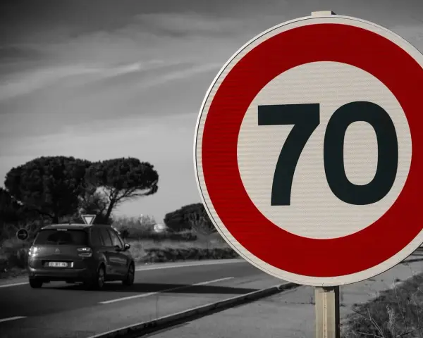 Segnale 226: limite di velocità 70. Un'auto viaggia su una strada panoramica.