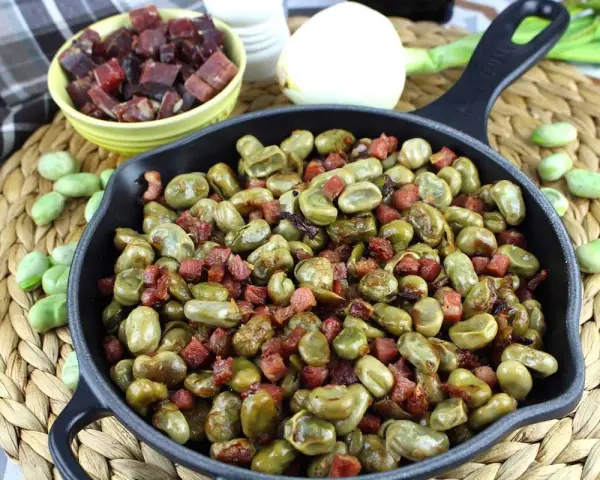 Habas tiernas salteadas con trocitos de jamón en una sartén de hierro fundido, un plato tradicional lleno de sabor.