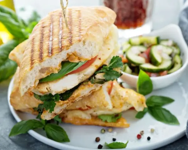 Pyszne panini z kurczakiem, pomidorem i bazylią, podane z sałatką z ogórka. Idealne na lekki posiłek.