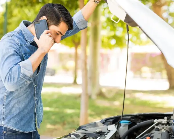 Mann telefoniert neben offenem Motorraum. Was ist beim Abschleppen zu beachten bei PKW Defekt?