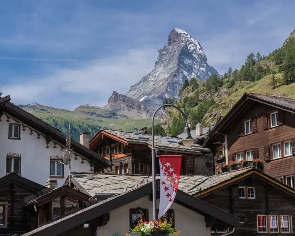 Tradycyjna winieta szwajcaria: drewniane domy z kamiennymi dachami i majestatyczny Matterhorn w tle.