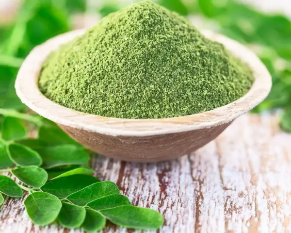 Zielony proszek z liści moringa w drewnianej miseczce, otoczony świeżymi liśćmi. Czy to ściema? Nie, to superfood!