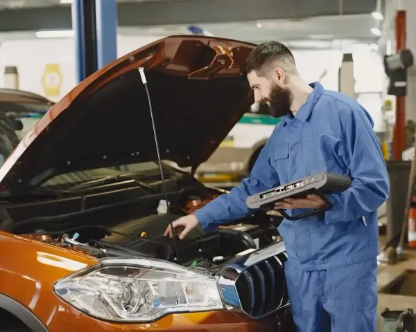Mechanik z komputerem diagnostycznym sprawdza silnik pomarańczowego auta. Zastanawiasz się, ile trwa wymiana oleju?