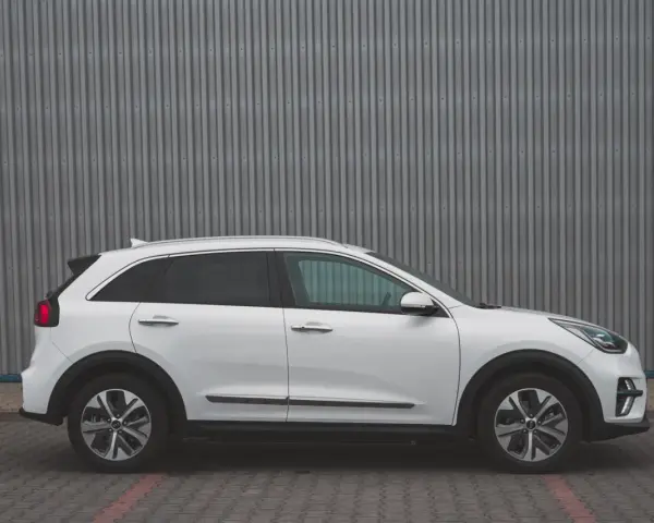 Biały Kia Niro EV widziany z boku na tle szarej, falistej ściany.