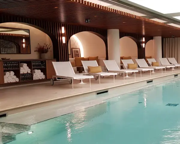 Piscine intérieure avec chaises longues blanches, coussins jaunes et étagères de serviettes.