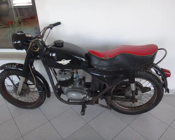 Czarny motocykl wsk 125 z czerwoną kanapą, stojący na szarej podłodze.