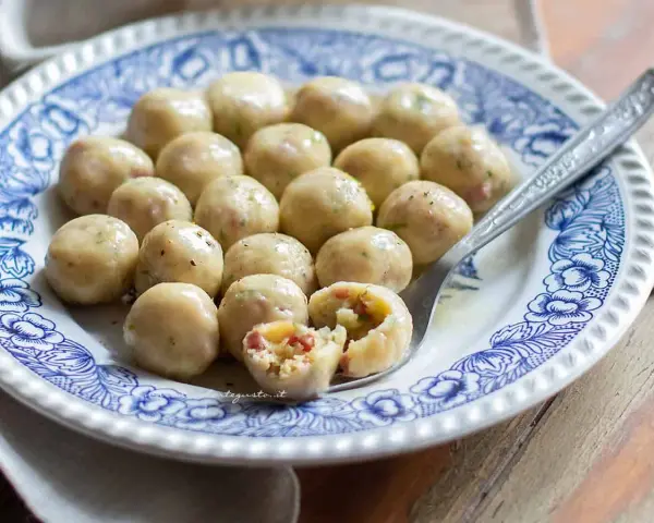 Gnocchi di pane saporiti, serviti su un piatto decorato. Uno è tagliato a metà, rivelando un ripieno gustoso.