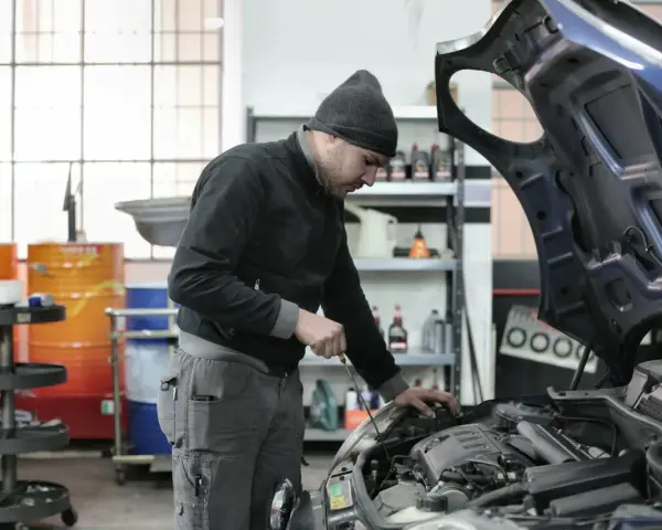 Mechanik w czapce z daszkiem sprawdza silnik. Zastanawiasz się, ile zarabia mechanik? Praca wymaga precyzji i wiedzy.