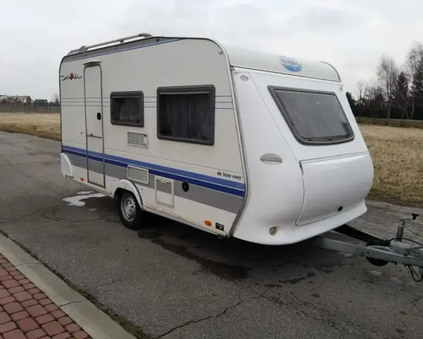 Biała przyczepa kempingowa Hobby 400 de luxe easy z niebieskimi pasami, gotowa na wakacyjne podróże.