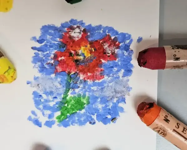 Apprenez comment utiliser les pastels à l'huile pour créer une fleur vibrante sur fond bleu. Des pastels jaune, rouge et orange sont visibles.