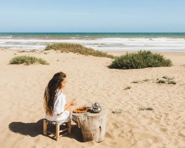 Kobieta pije herbatę na piaszczystej plaży, delektując się widokiem na turkusowe tunezyjskie morze.