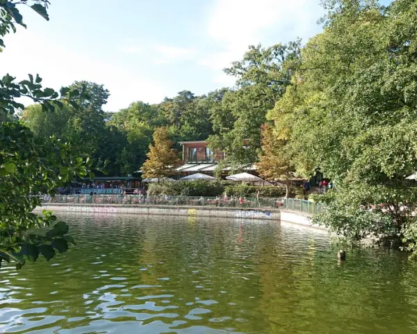 Grüne Bäume säumen den Schlachtensee Berlin, wo Menschen auf der Terrasse eines Restaurants sitzen.