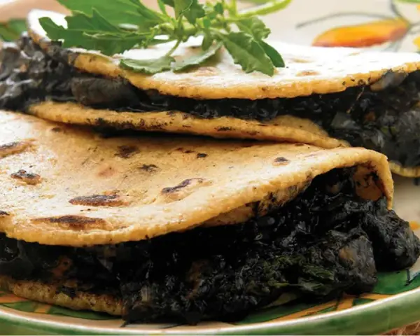 Dos tortillas de maíz rellenas de quelites, un platillo que evoca lo que comían los aztecas.