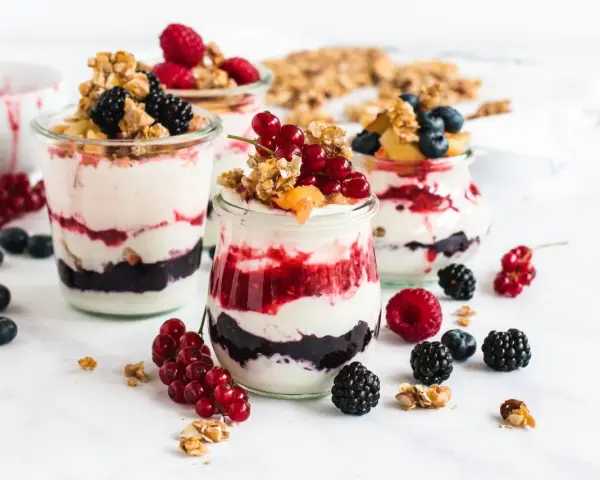 Leckeres Dessert mit Beeren und Joghurt in Gläsern geschichtet, garniert mit Granola und frischen Früchten.