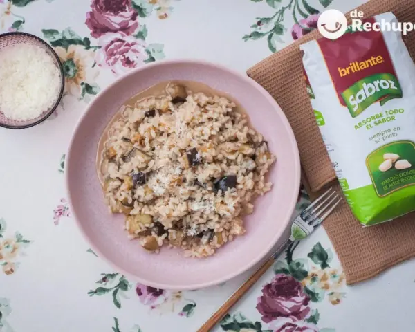 Arroz meloso con berenjenas en plato rosa, acompañado de queso rallado y bolsa de arroz Sabroz.