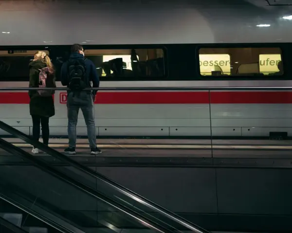 Para stojąca na peronie przed pociągiem, obok schodów ruchomych.