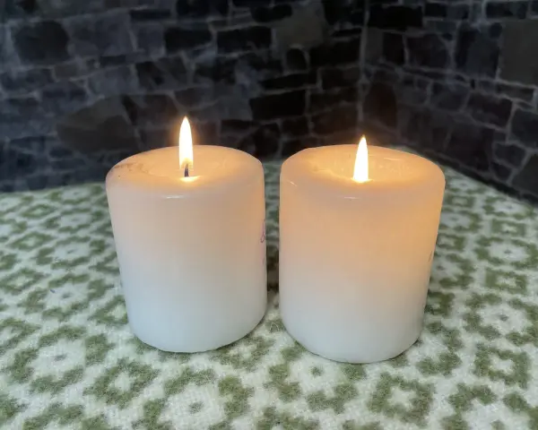 Two white candles glow softly, their flames flickering. This peaceful scene evokes the second Sunday of Advent theme of hope and preparation.