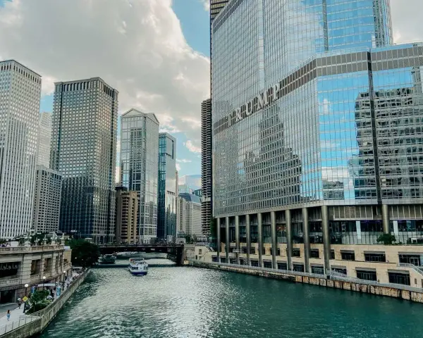 Chicago's iconic skyline along the river, with the Trump Tower reflecting the clouds. A boat glides by, making you wonder, is Chicago worth visiting?