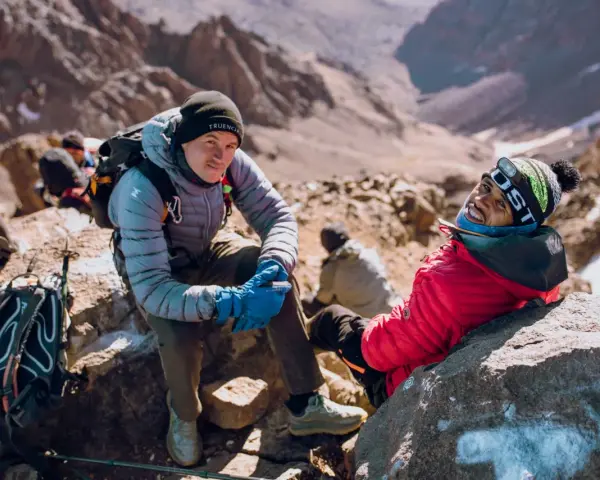 Uśmiechnięci alpiniści podczas wyprawy na Toubkal. W tle skaliste zbocza górskie.