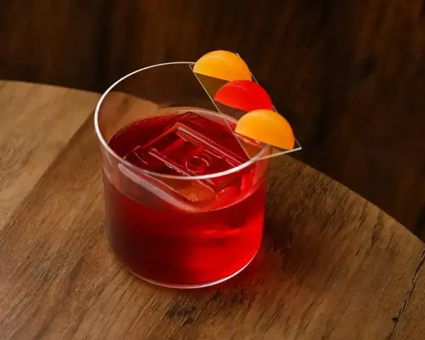 Klasyczny negroni przepis: czerwony koktajl z lodem i pomarańczową dekoracją na drewnianym blacie.