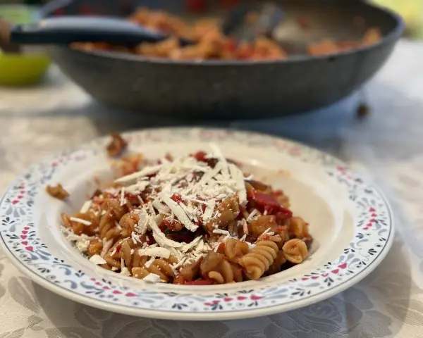 Plato de pasta alla norma con fusilli, berenjena, tomate y queso rallado, listo para disfrutar.