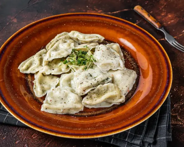 Talerz pełen pierogów, które przypominają o tradycji i pytają skąd pochodzą pierogi. Zioła dodają świeżości.