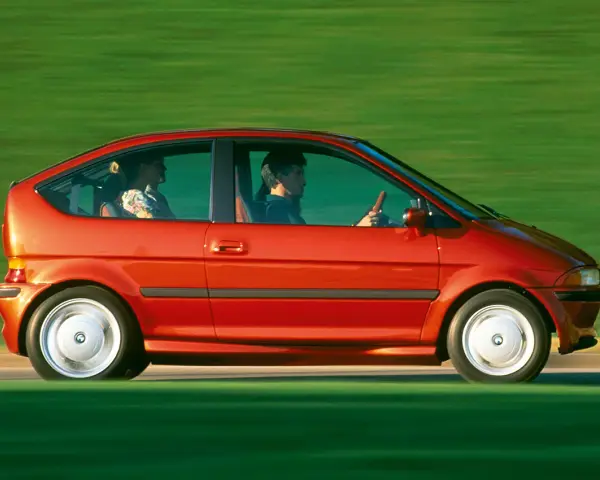 Czerwony samochód elektryczny BMW E1 z lat 90. jadący po zielonym tle.