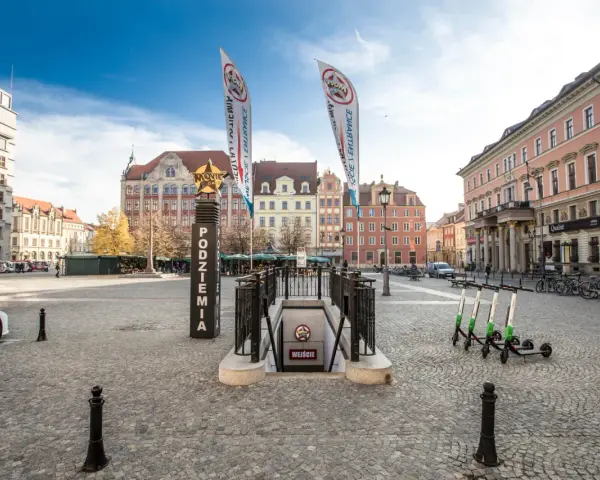 Wejście do podziemi z napisem "Movie Gate Wrocław" na placu w otoczeniu zabytkowych kamienic.