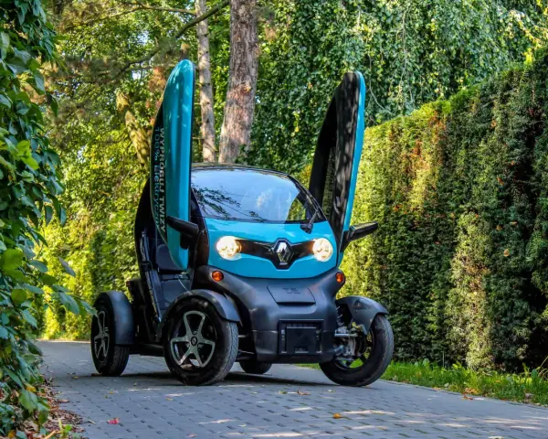 Niebieski Renault Twizy z otwartymi drzwiami stoi na ścieżce wśród zieleni.