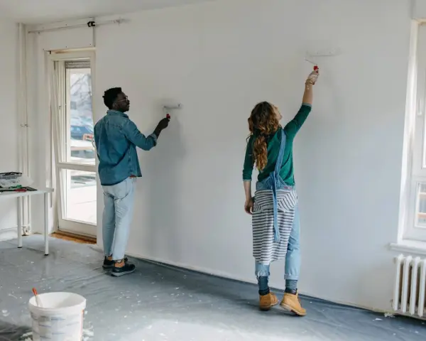 Pareja pintando una pared blanca, renovando su hogar. El hombre y la mujer usan rodillos para pintar sobre lacado, transformando el espacio.