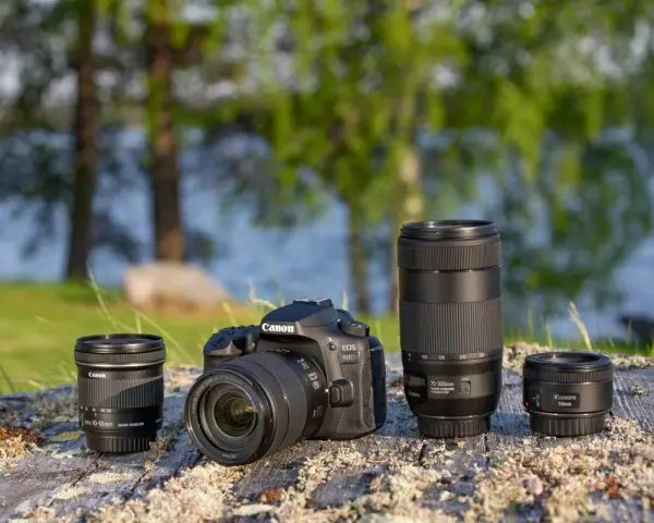 Aparat Canon EOS 90D z obiektywami 10-18mm, 70-300mm i 50mm na kamieniu nad jeziorem.