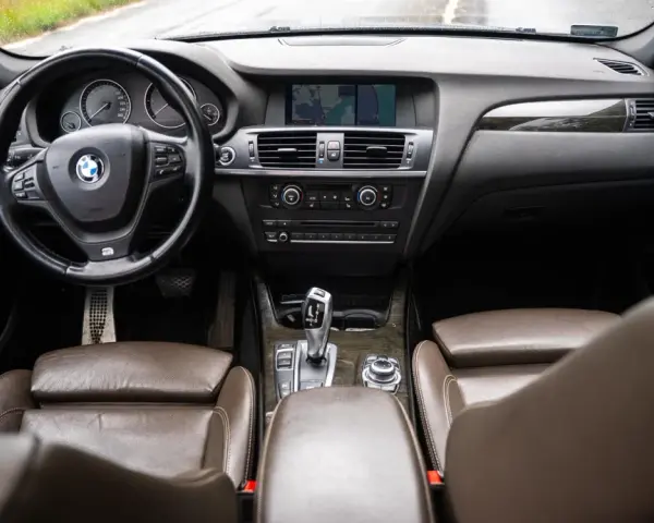 Wnętrze BMW X3 z brązową skórzaną tapicerką i drewnianymi wstawkami. Kierownica, deska rozdzielcza i nawigacja. Wiele osób szuka bmw x3 opinie, by poznać ten model.